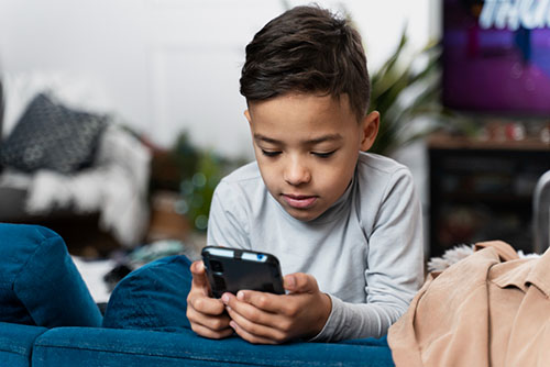 Mobile addiction in children – boy looking at smartphone screen indoors